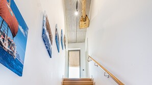 A wooden staircase with a handrail, leading to a room with a concrete ceiling and a door with vertical blinds. - 360° Apartmenthotel - by teamgeist (Heidesee)