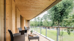 A wooden deck with wicker furniture and a view of a grassy area. - 360° Apartmenthotel - by teamgeist (Heidesee)