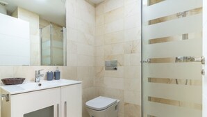 Un baño moderno con cabina de ducha de vidrio, un lavamanos blanco con espejo y un inodoro.