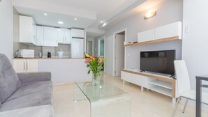 Una sala de estar moderna con una mesa de centro de vidrio, un sofá gris, un televisor de pantalla plana y un mueble bajo de madera.
