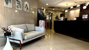 A reception area with a sofa, a desk, and a vase of flowers. - The Snooze Hotel Bugis (Singapore)
