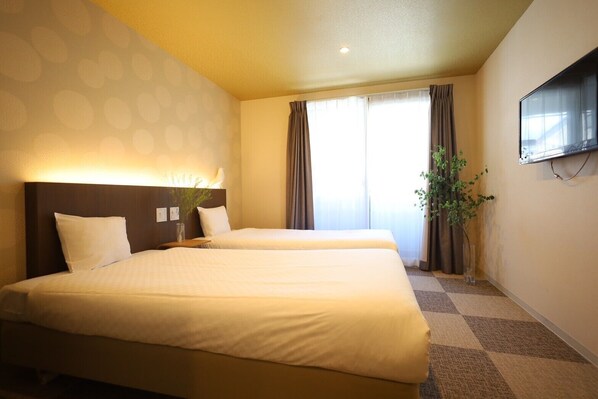 Une chambre d’hôtel avec deux lits, un téléviseur à écran plat fixé au mur et une grande fenêtre avec des rideaux.