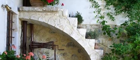An outdoor patio with a stone archway, wooden furniture, and potted plants.