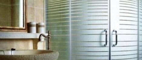 Une salle de bain dotée d’une douche ronde en verre, d’un miroir rond et d’un lavabo beige avec un plan de travail en pierre.