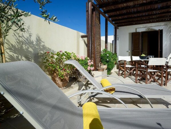 A sunlit outdoor seating area with lounge chairs and a table, surrounded by potted plants and a pergola structure. - Villa Agriolive (Hersonissos)