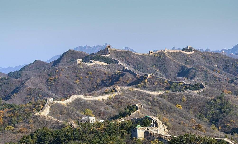 Paisaje montañoso con una muralla histórica y torres de vigilancia.