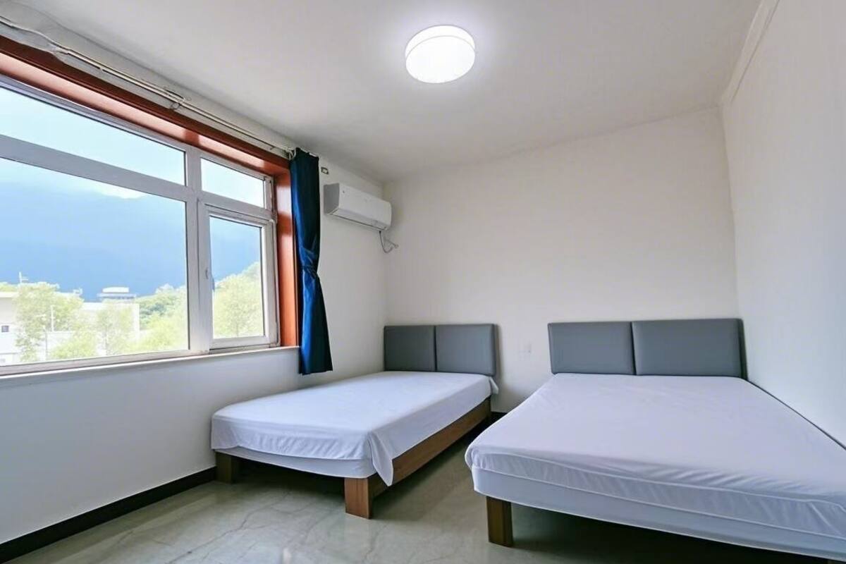 Habitació amb dos llits individuals, una finestra amb cortines, aire condicionat i vista al mar.