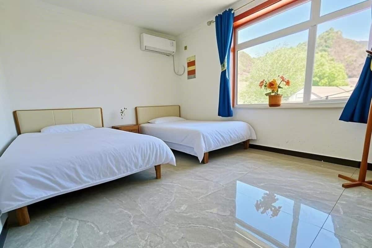 Habitació d'hotel amb dos llits, una finestra gran amb cortines, una planta en test i un sòl de rajola.