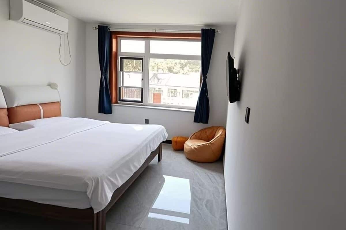 Una habitació d'hotel moderna amb un llit gran, una finestra amb cortines, un televisor de pantalla plana i un seient informal de cuir.
