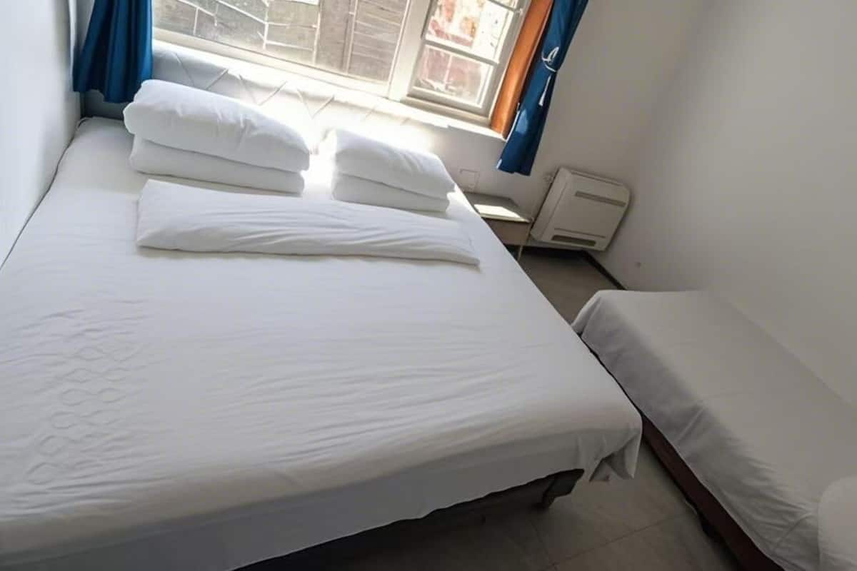 Habitació individual amb un llum gran, un radiador i una cortina blava.
