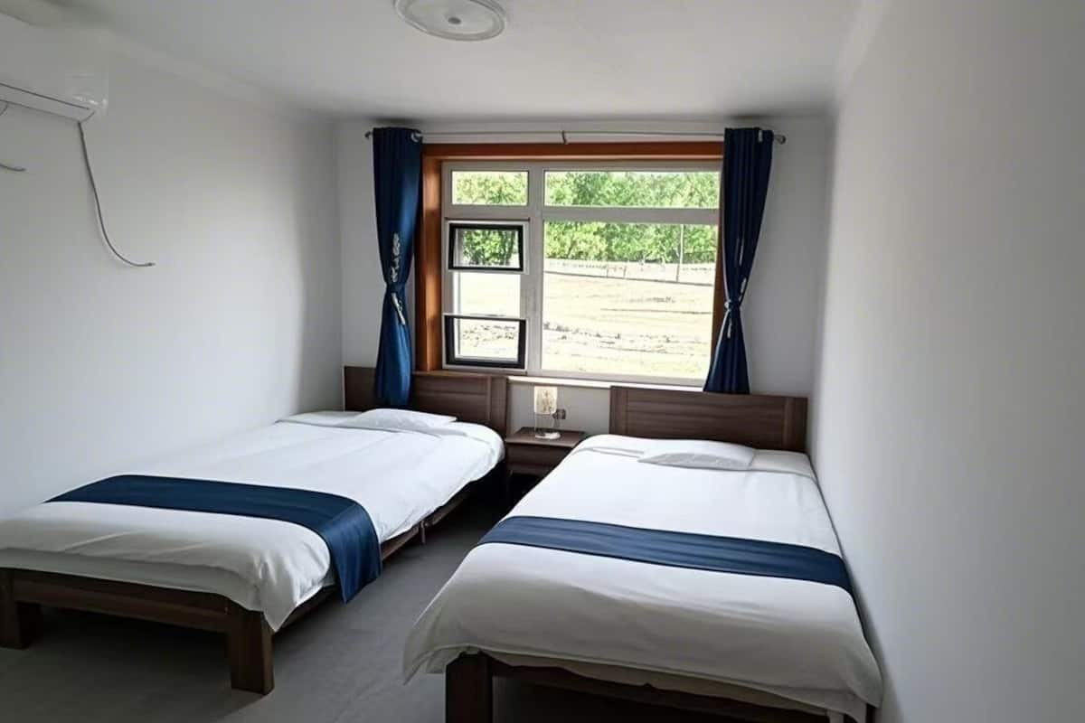 Una habitació amb dos llits individuals, una taula petita i una finestra amb cortines.