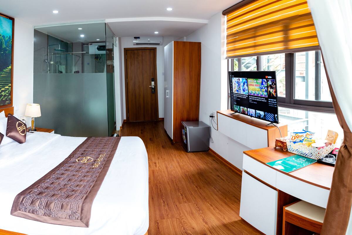 Une chambre d’hôtel avec un grand lit, une télévision, un bureau et une fenêtre avec des stores.