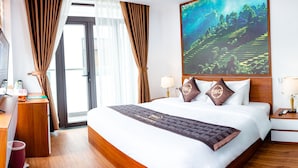 Een hotelkamer met een groot bed, een bureau met computer, een raam met gordijnen en een schilderij van een landschap.