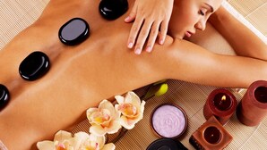 Iemand ontvangt een rugmassage met stenen en bloemen op een mat.