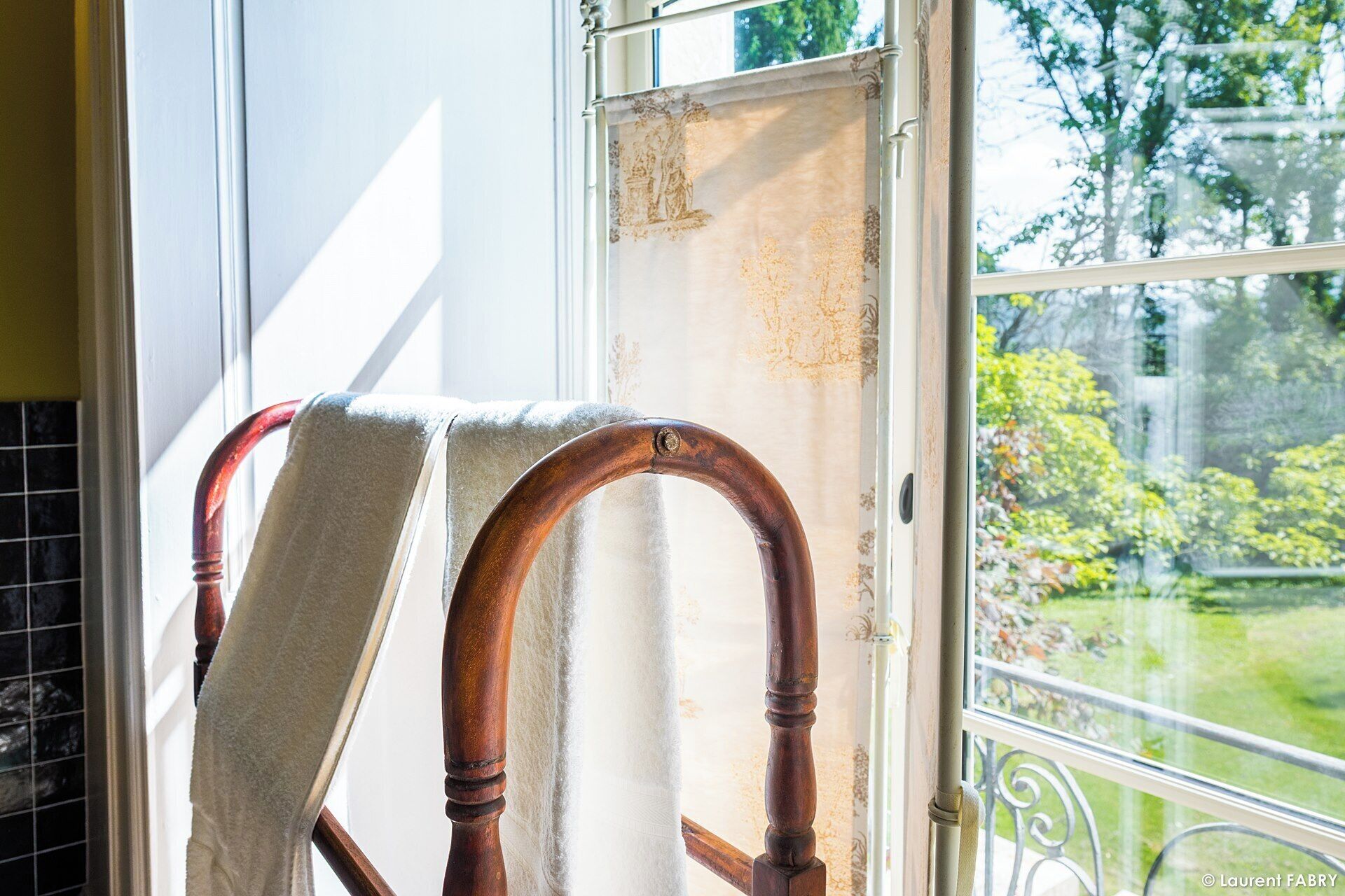 A wooden chair with a towel draped over it, positioned near a window with a view of greenery outside.
