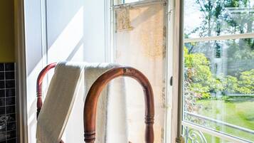 A wooden chair with a towel draped over it, positioned near a window with a view of greenery outside.