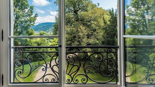 A balcony with wrought iron railings and a view of a lush green landscape with trees and hills. - Chateau de Maillat (Maillat)