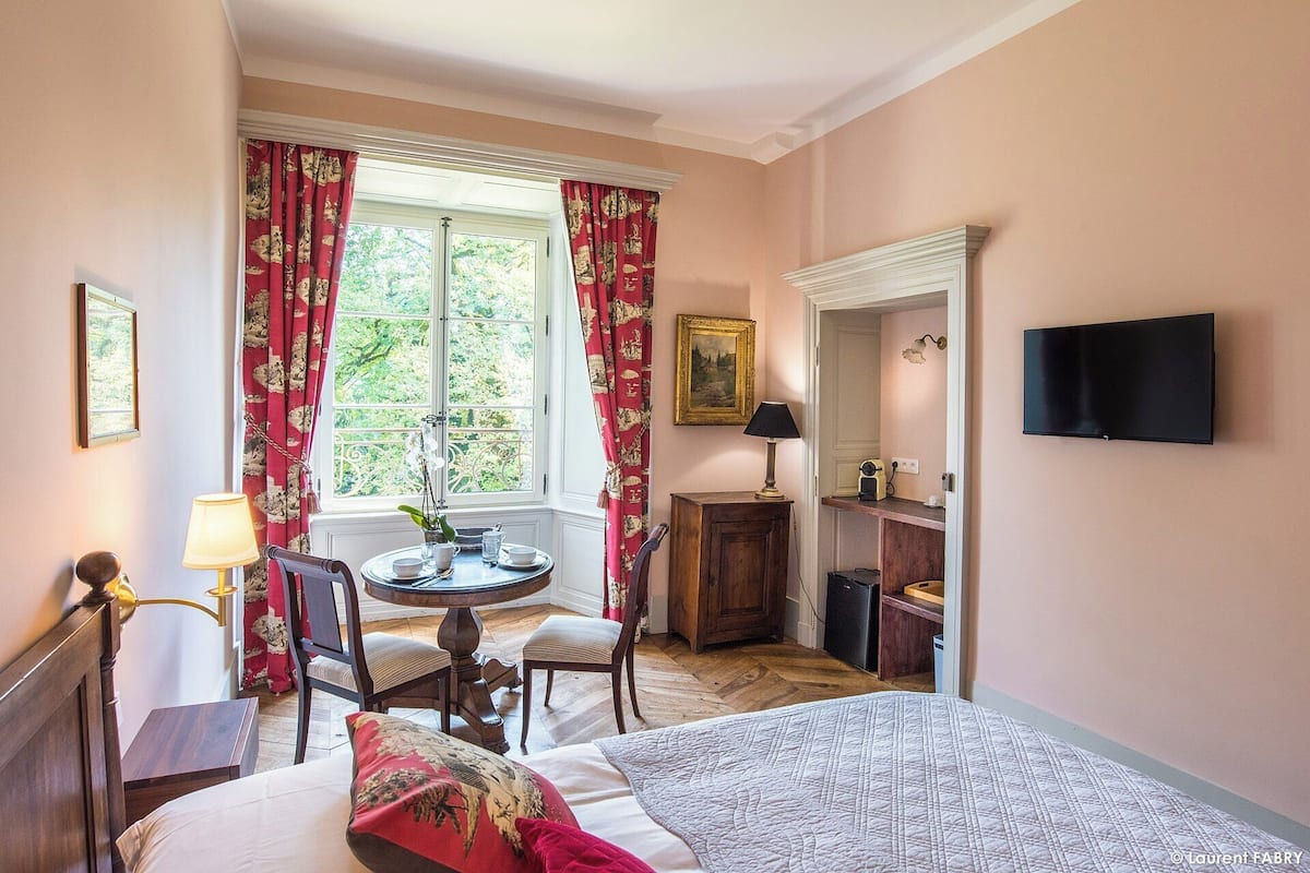 Habitació d'hotel amb un llit, escriptori amb cadira, taula petita amb làmpada, televisió i finestra amb cortines.