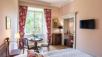 Habitación de hotel con cama, escritorio y silla, una mesita con lámpara, televisión y ventana con cortinas.