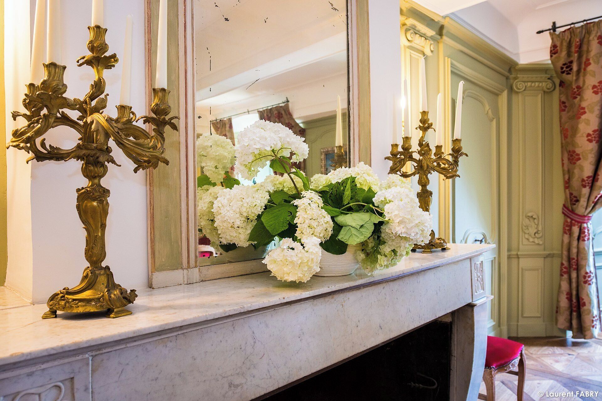 Una mensola del camino in marmo con un vaso di fiori bianchi e due elaborati candelabri.