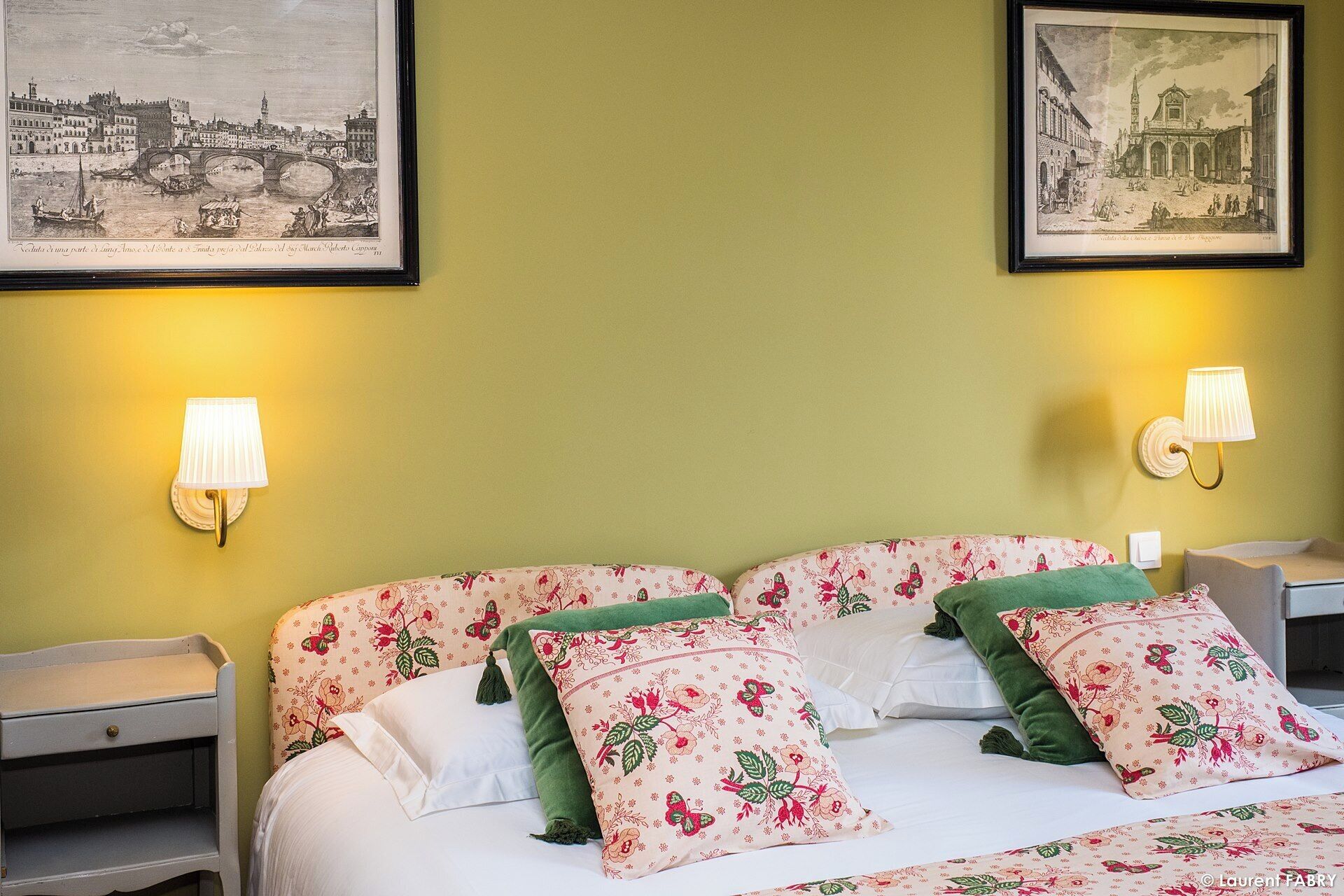 Una camera d'albergo con un letto, due comodini, due lampade a parete e due quadri appesi alla parete.