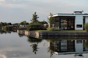 A modern building with large windows, a reflection in the water, and a small bridge in the background. - Loosdrecht Water Villa (Nieuw-Loosdrecht)