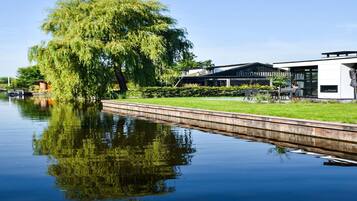 A calm river with a weeping willow tree and a modern building with a glass facade.