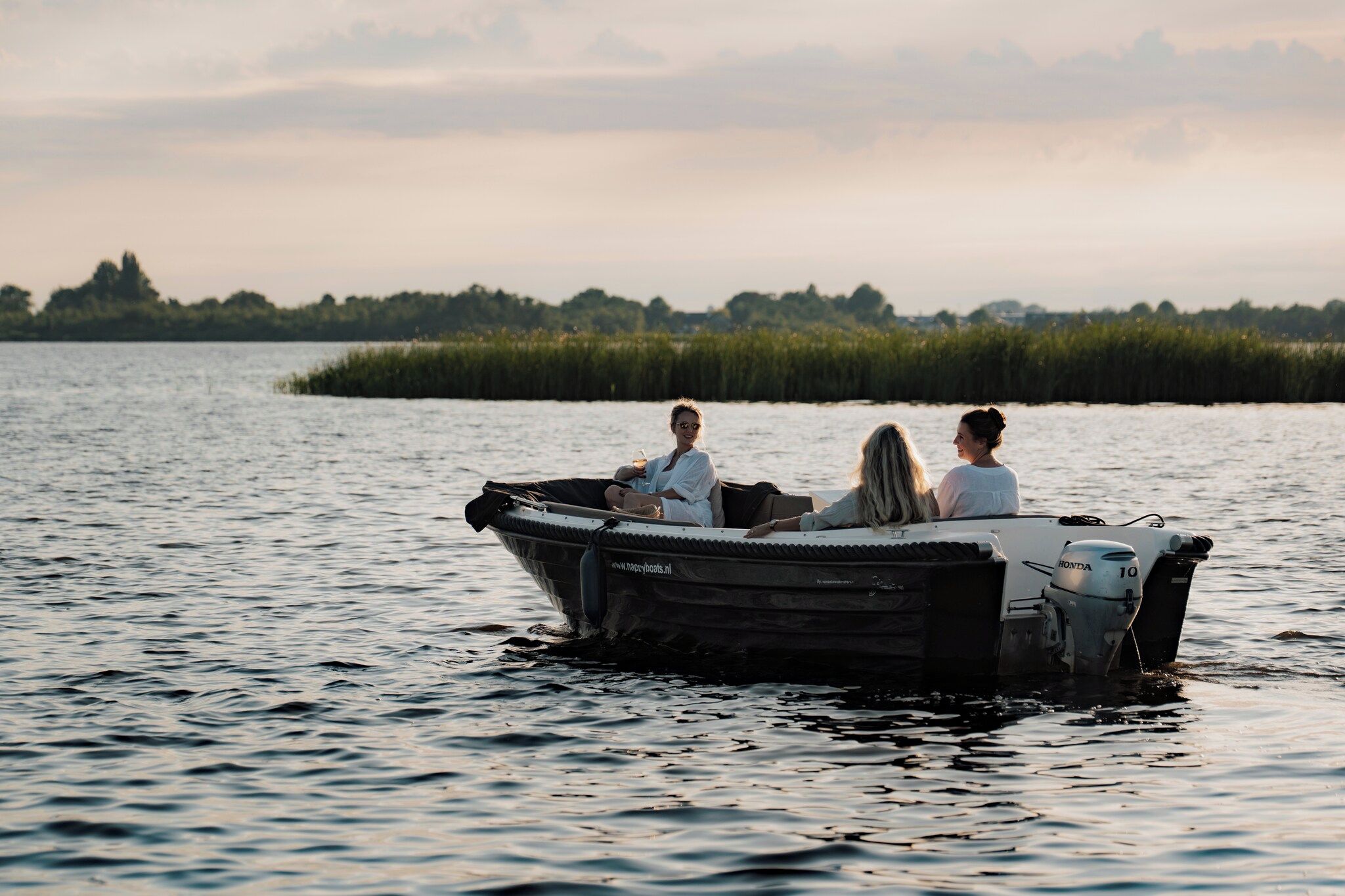 Un petit bateau à moteur avec trois personnes à bord, naviguant sur une étendue d’eau dont la côte est visible au loin.