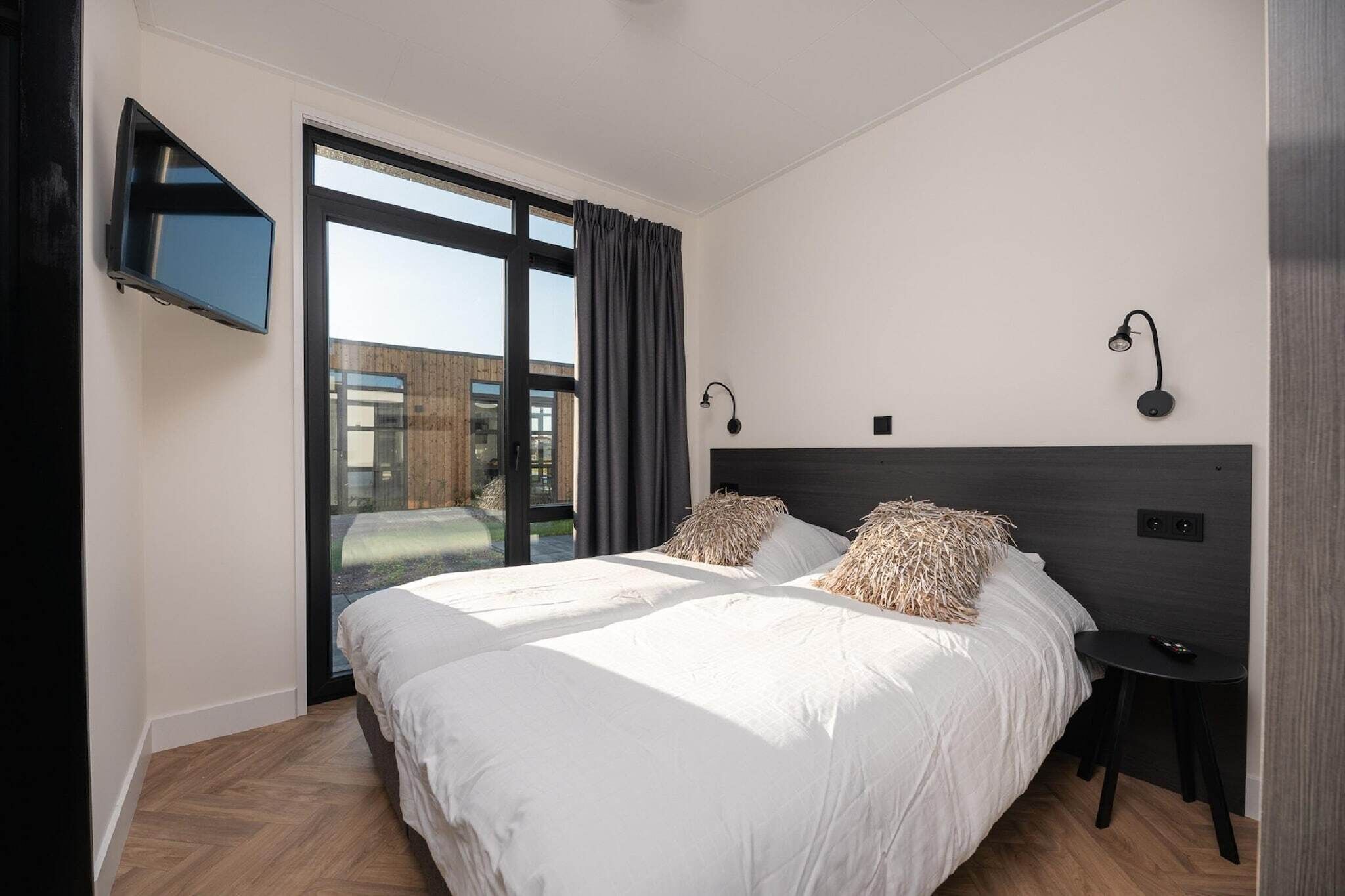 A modern bedroom with a large bed, a TV mounted on the wall, and a view of the outside.