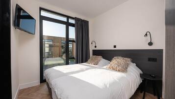 A modern bedroom with a large bed, a TV mounted on the wall, and a view of the outside.