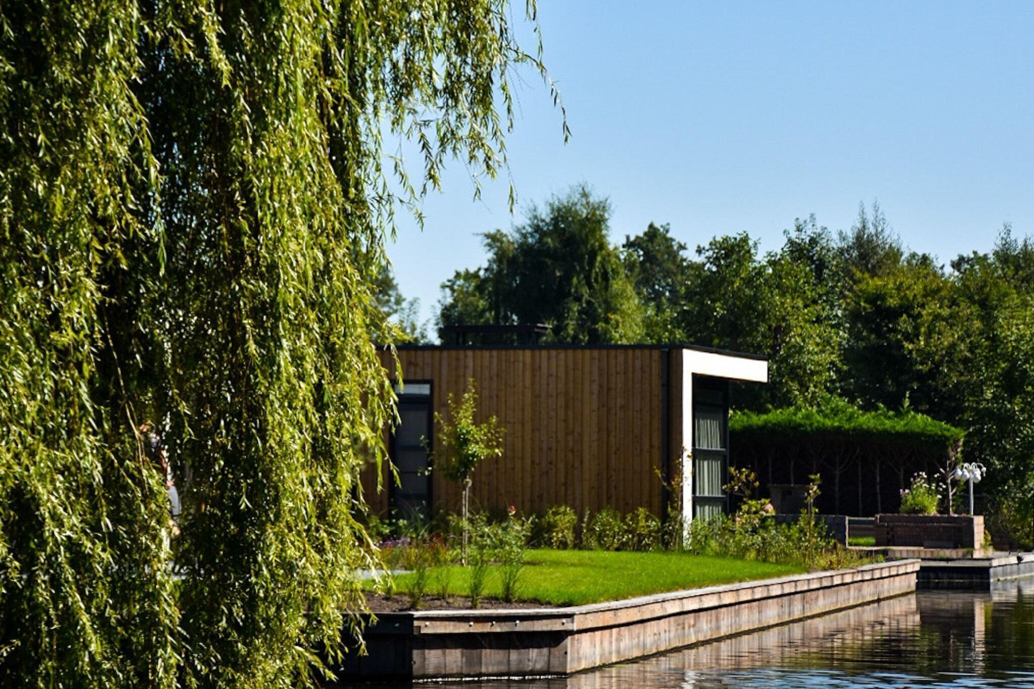Un bâtiment moderne avec une façade en bois, un espace verdoyant et un plan d’eau au premier plan.