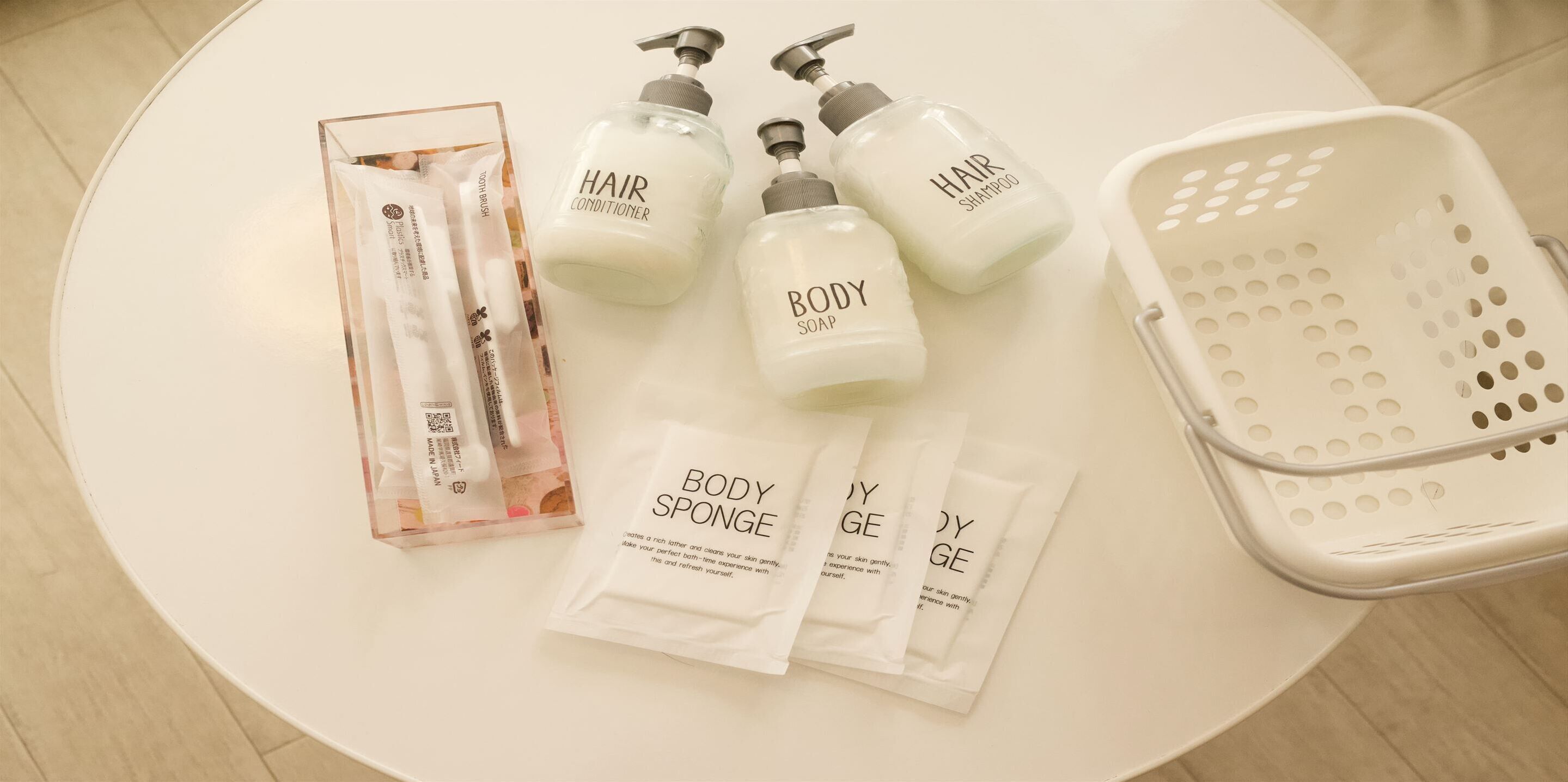 A white table with various personal care products including hair conditioner, body soap, shampoo, and body sponge packets.