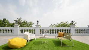 A rooftop terrace with a white balustrade, two white chairs, a yellow bean bag, and a small round table. - Cove Veranda (Jakarta)
