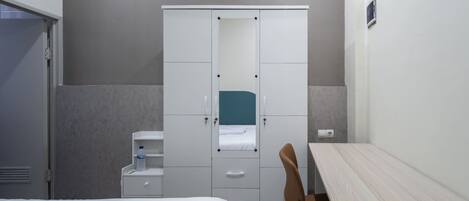 A compact hotel room with a bed, a wardrobe, a desk, and a chair.