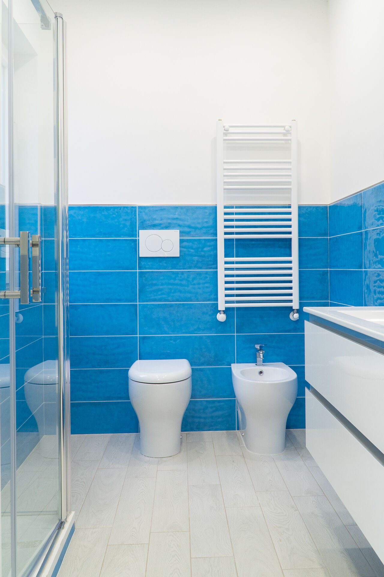 A bathroom with two toilets, a bidet, a glass shower enclosure, and a white sink.