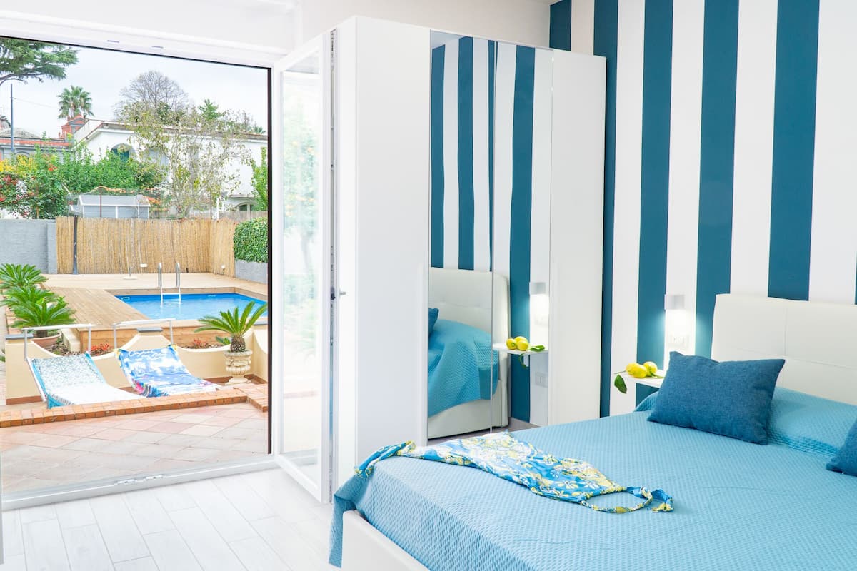 A modern bedroom with a large bed, a view of a swimming pool, and a sliding glass door leading to an outdoor area.