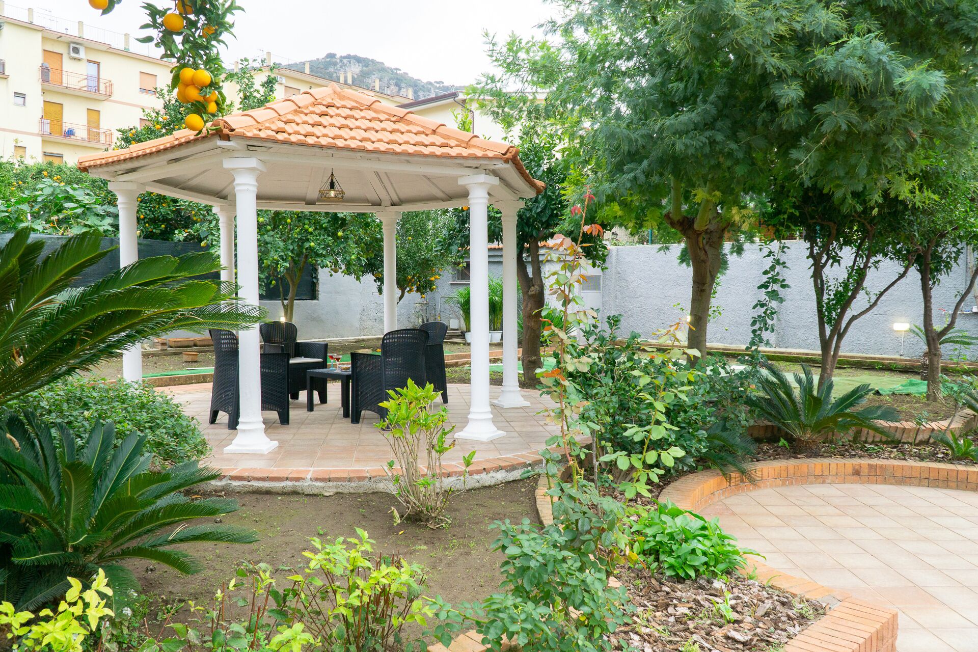 A covered outdoor seating area with chairs and tables, surrounded by lush greenery and a view of a body of water.