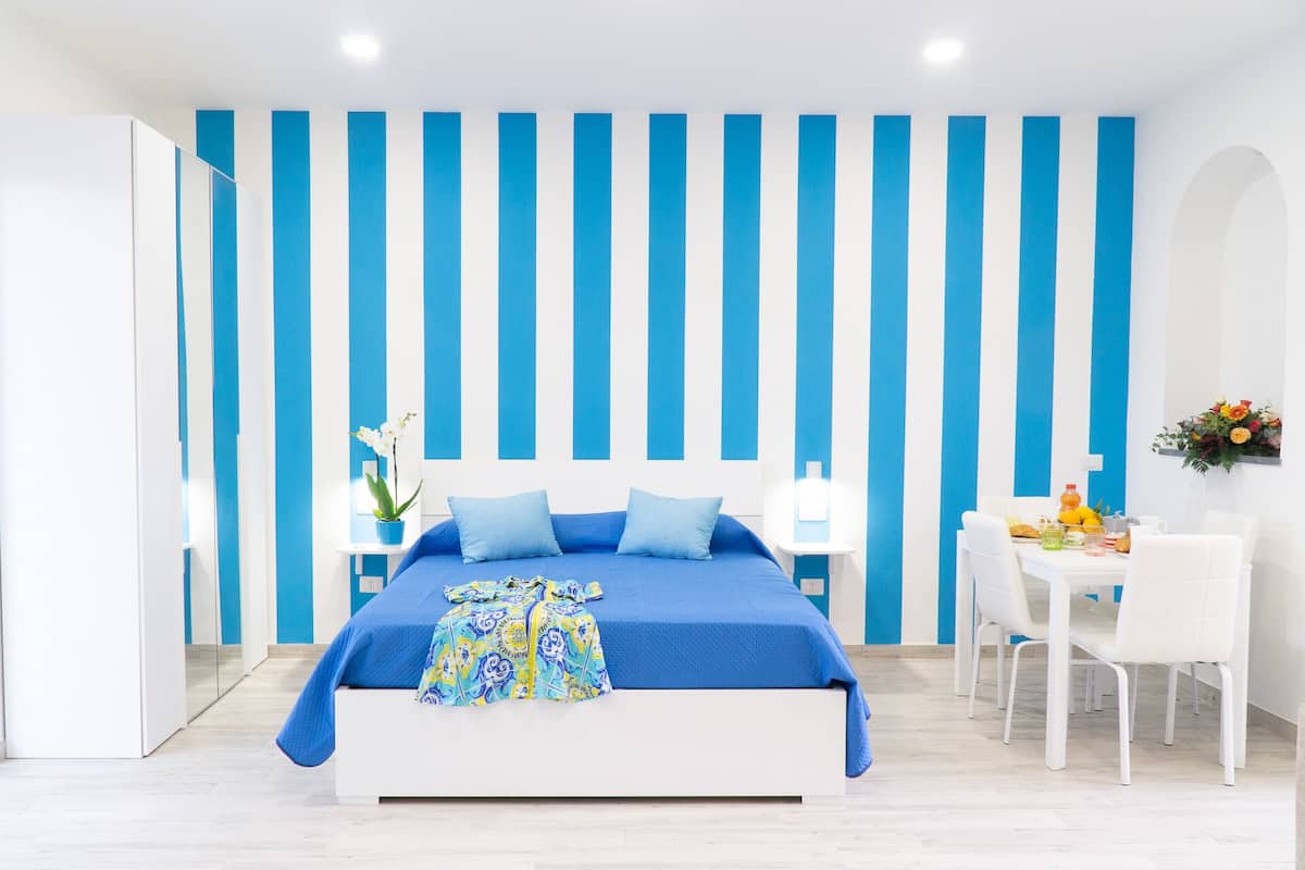 A modern bedroom with a bed, bedside table, and a small dining area with chairs and a table.
