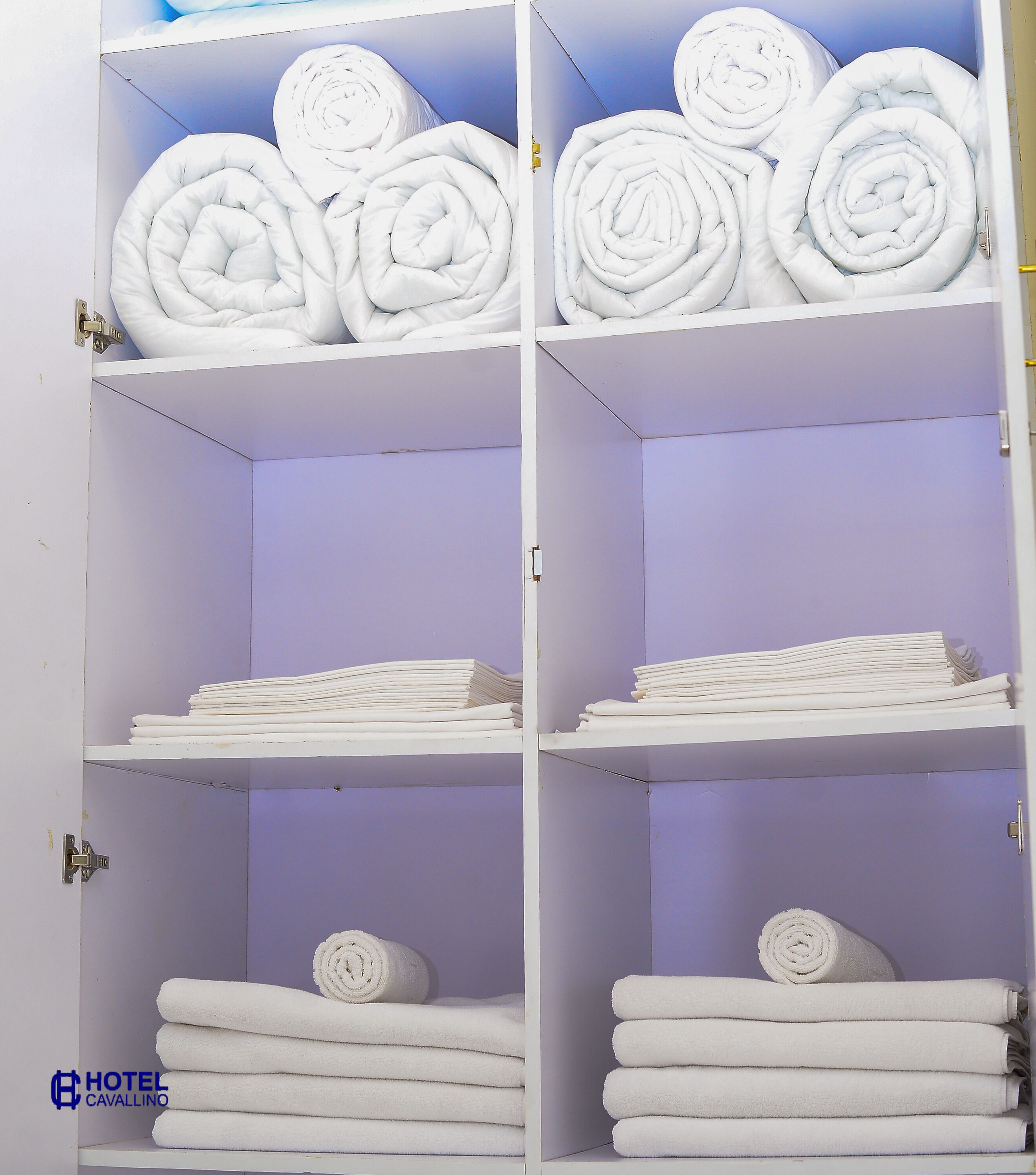 A hotel storage room with shelves containing neatly folded towels and rolled bathrobes.