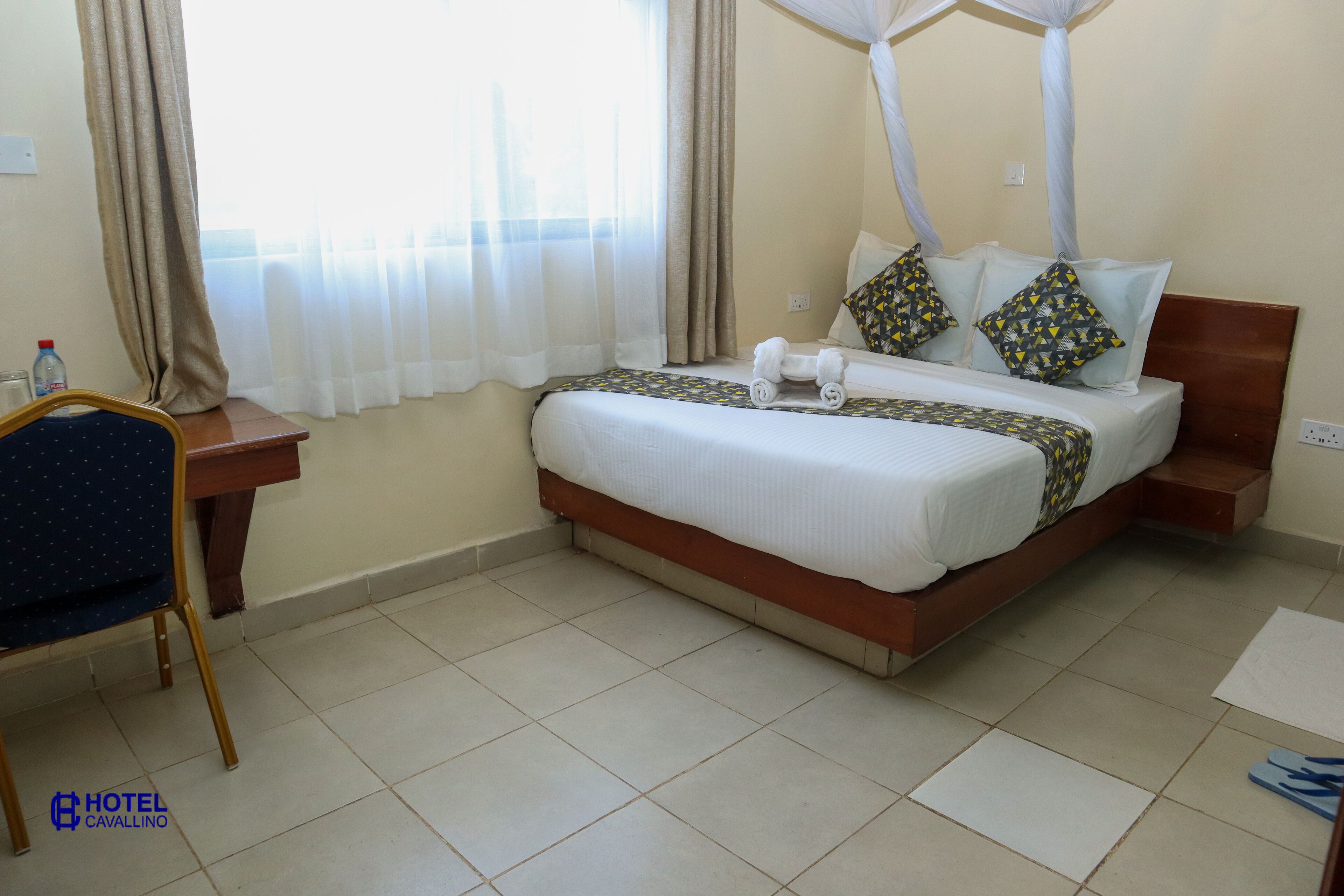 A hotel room with a bed, a desk, a chair, and a window with curtains.