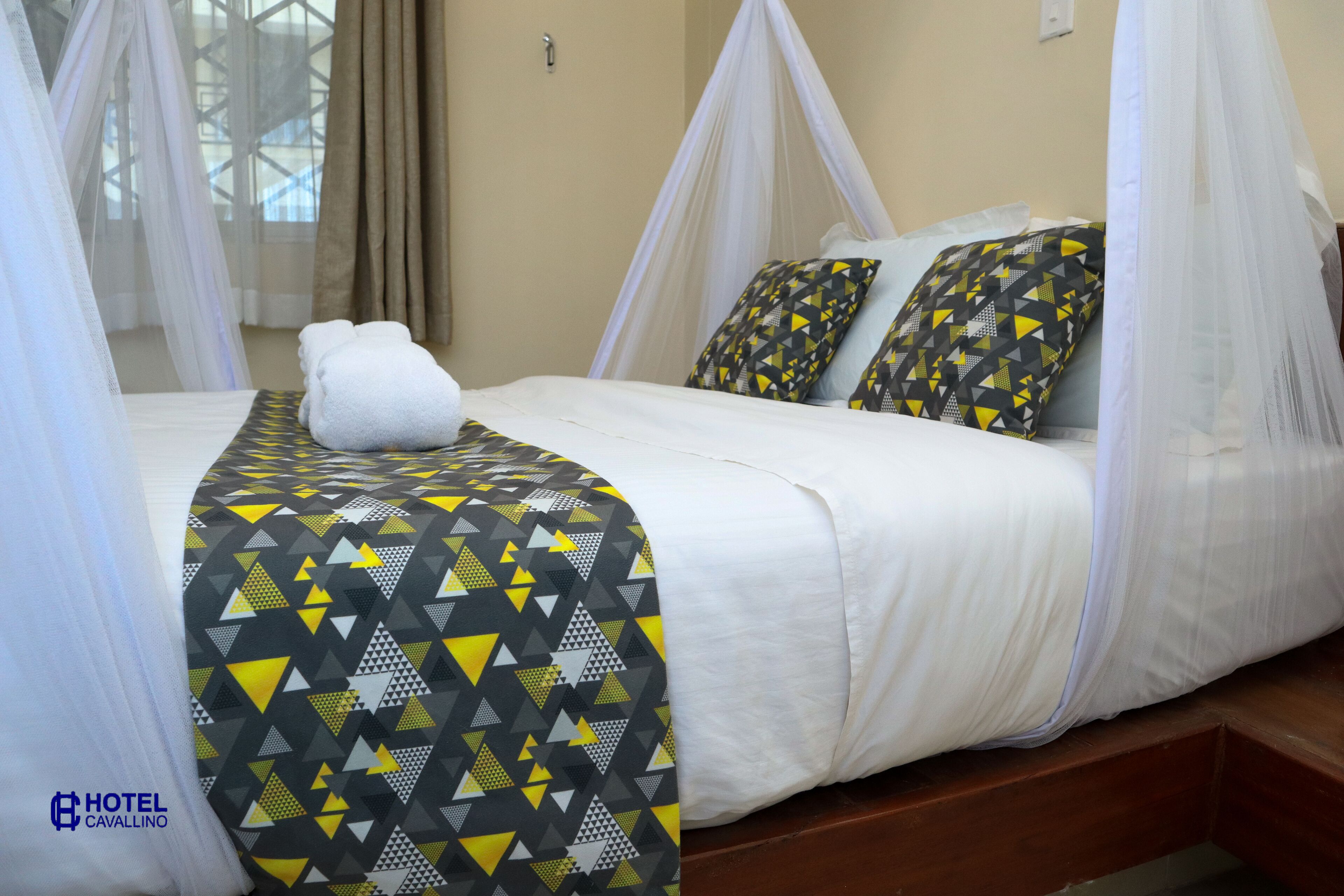 Quarto de hotel com cama, roupa de cama branca, manta de padrão geométrico e cama com dossel.