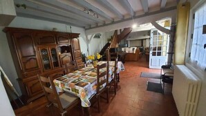 A dining area with a wooden table and chairs, a cabinet, and a staircase leading to another room. - La Chaumière aux Lamas (Goupil-Othon)