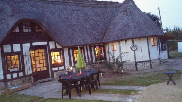 A traditional thatched-roof house with a dining area featuring a table and chairs. - La Chaumière aux Lamas (Goupil-Othon)