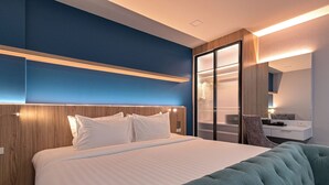 A modern hotel room with a large bed, a tufted armchair, a wooden headboard, and a glass partition. - Shewin de Bangkok (Bangkok)