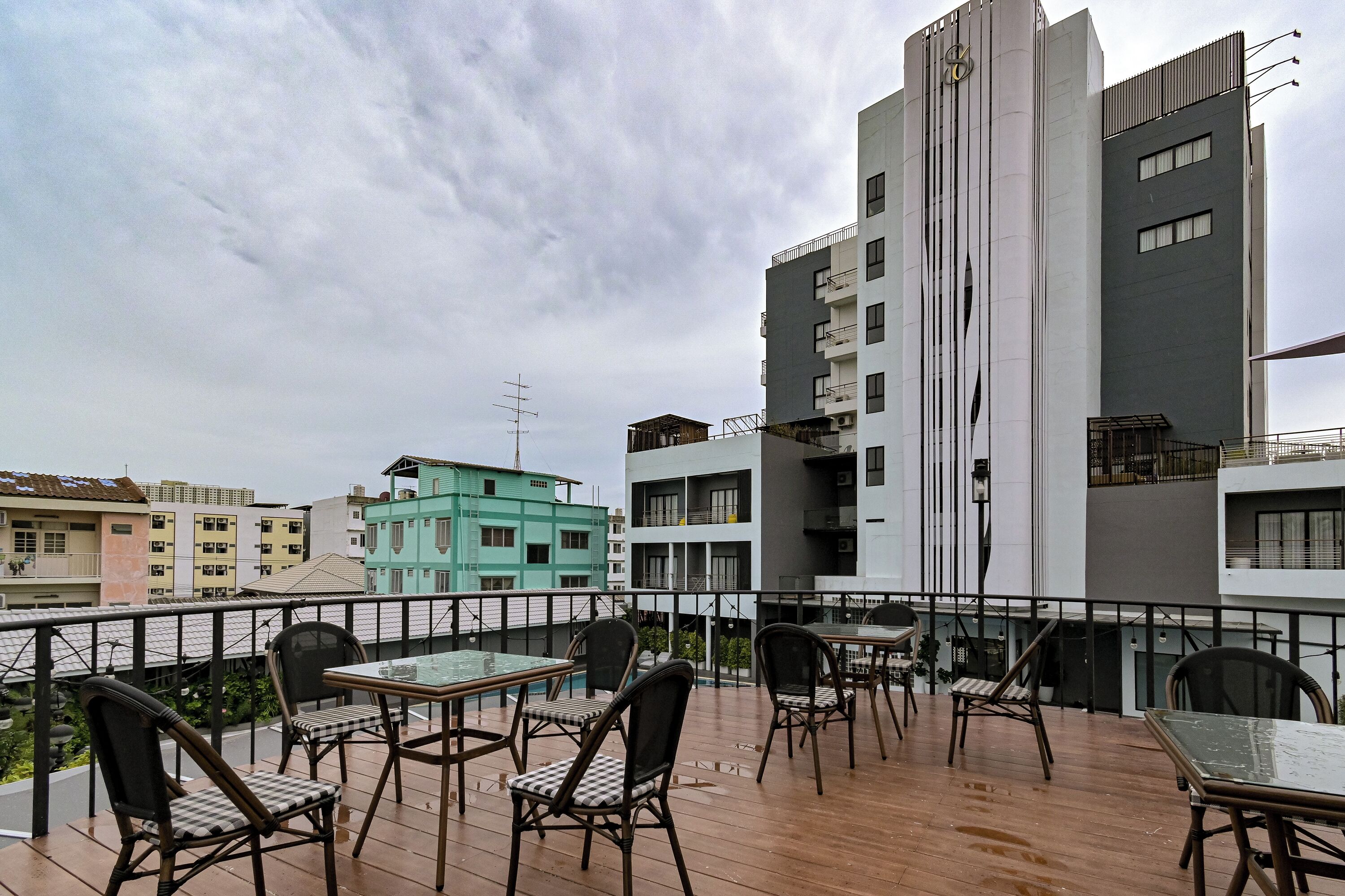 Una terraza en la azotea con mesas y sillas, una piscina y vistas de edificios circundantes.