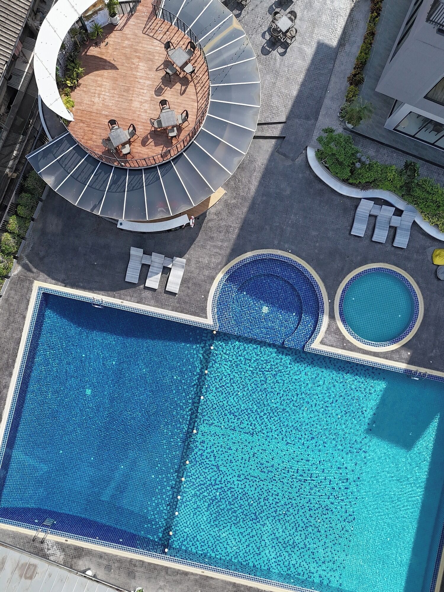 Vista aérea de un hotel con una piscina grande, una terraza con sol y asientos, y una zona ajardinada con plantas.