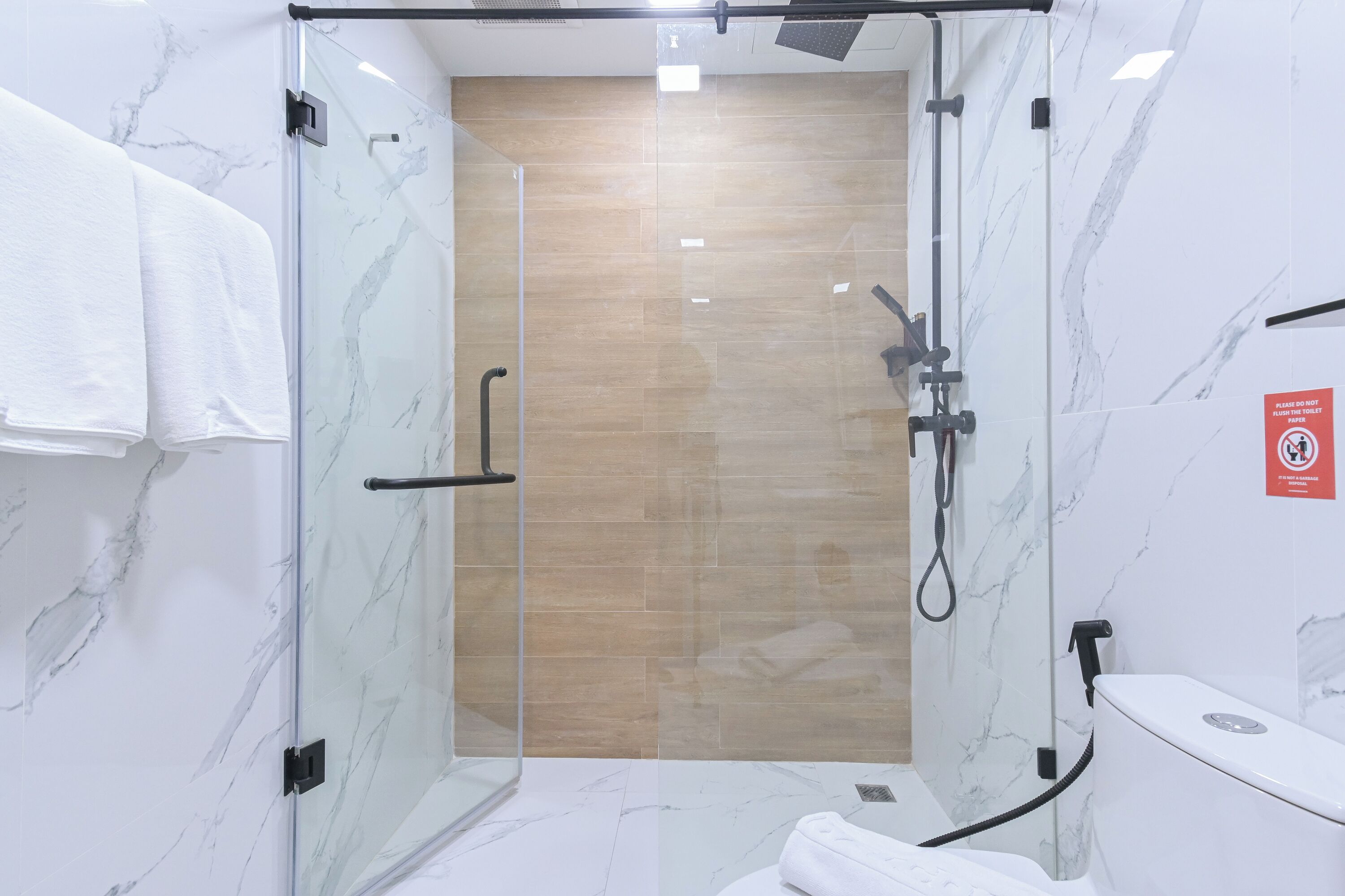 Un baño moderno con cabina de ducha de vidrio, paredes de mármol y suelo de madera.