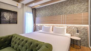 Un dormitorio moderno con una pared de acento de piedra, un sofá verde capitonado, una cama grande con ropa blanca y una pequeña mesa redonda.