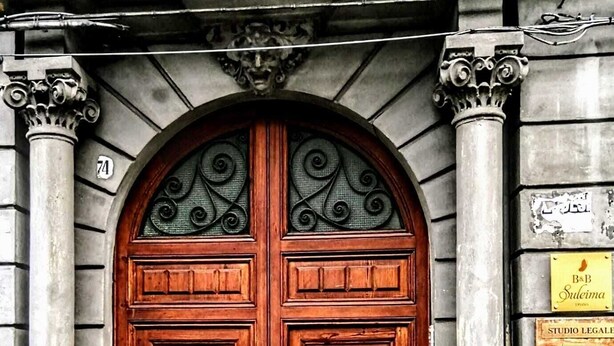 Una doble puerta de madera con una reja de metal, flanqueada por columnas y una placa con el nombre "B&B Sueleima" en la pared.