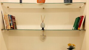 Una habitación con tres estantes de vidrio, cada uno con libros, un objeto decorativo y una pequeña planta en maceta.